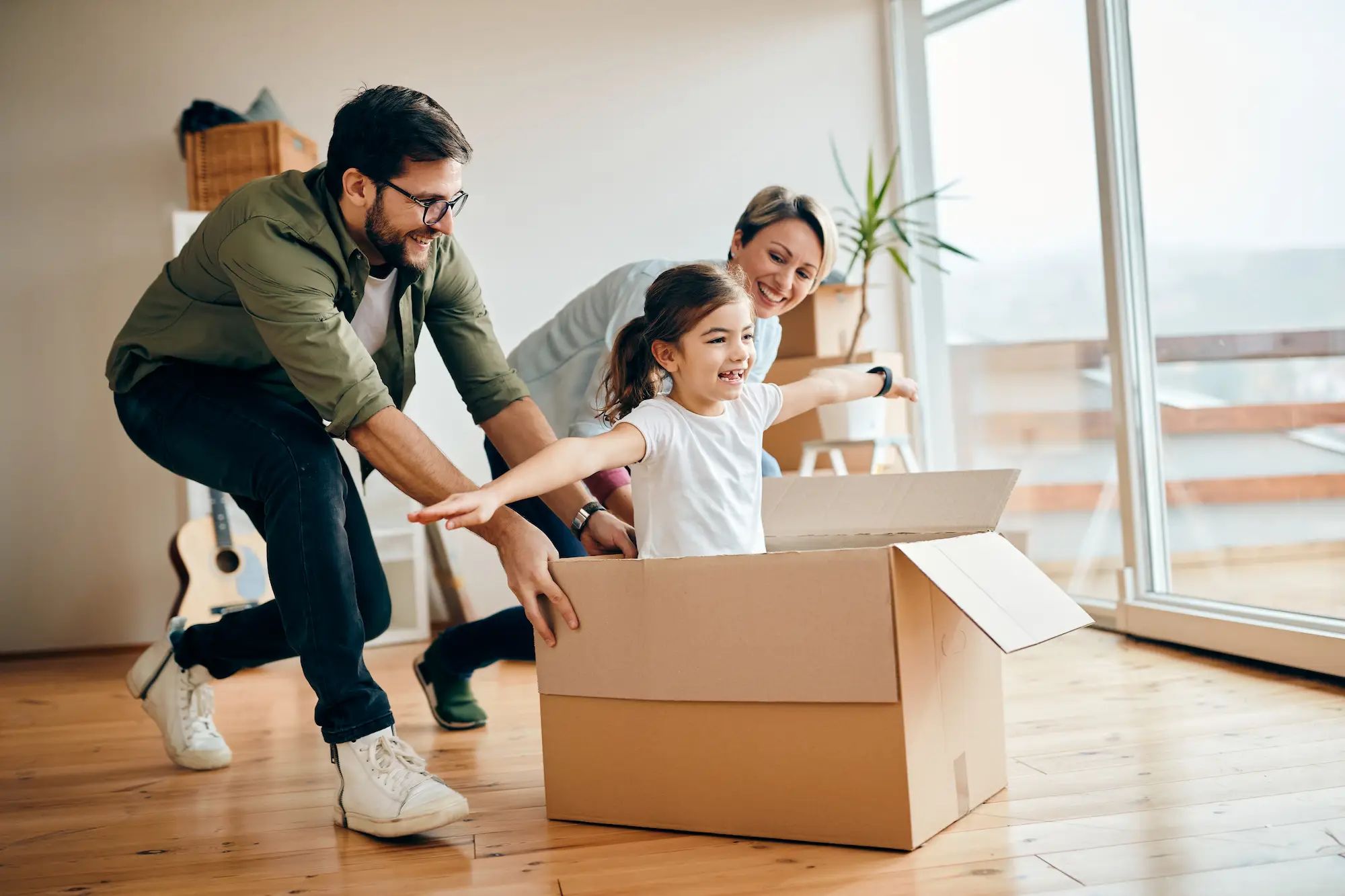 Parents pushing a box with kid inside pretending to fly.